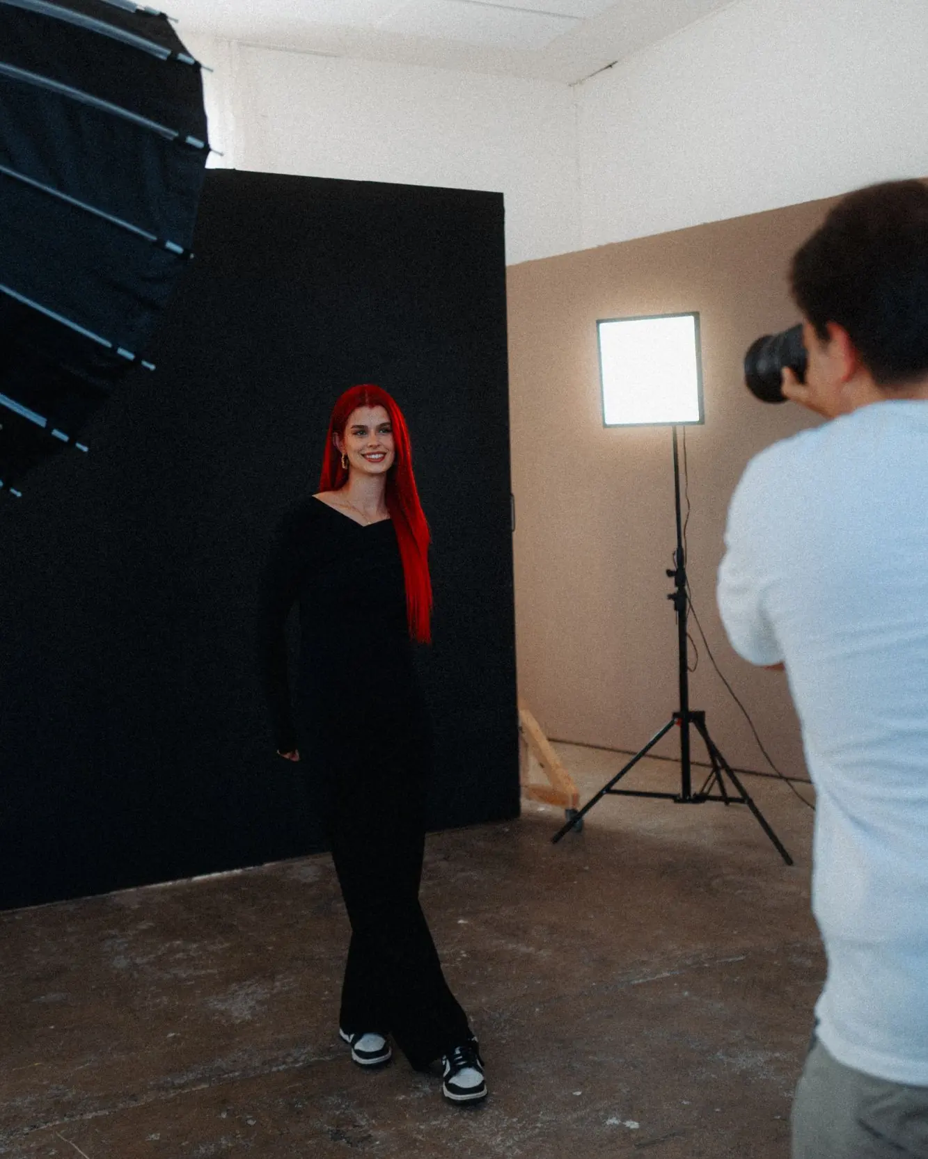 Eine Frau mit langen roten Haaren steht lächelnd vor einem dunklen Hintergrund und wird im Studio fotografiert