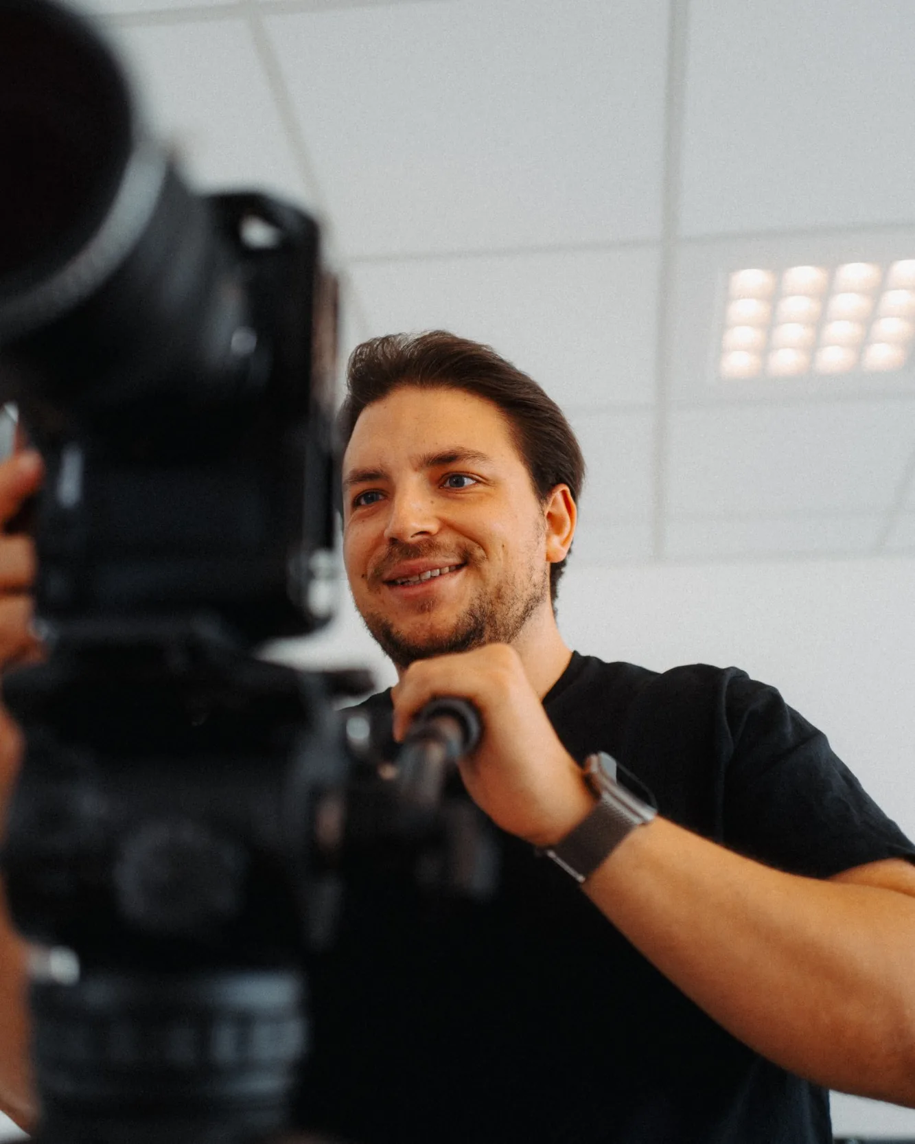 Nick Paysan lächelt hinter einer Kamera auf dem Stativ