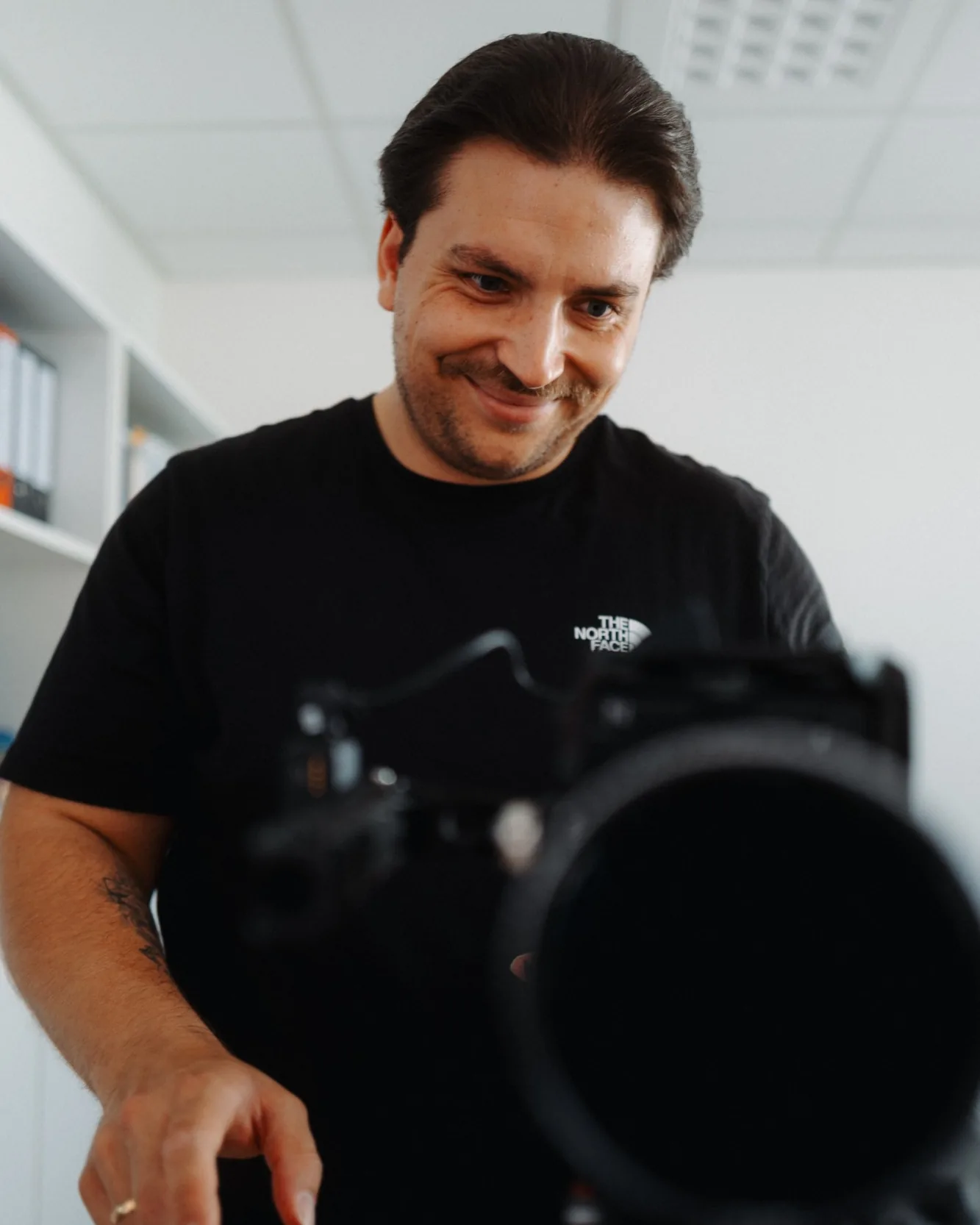 Nick Paysan steht im schwarzen T-Shirt lächelnd an seiner Kamera und blickt auf das Display