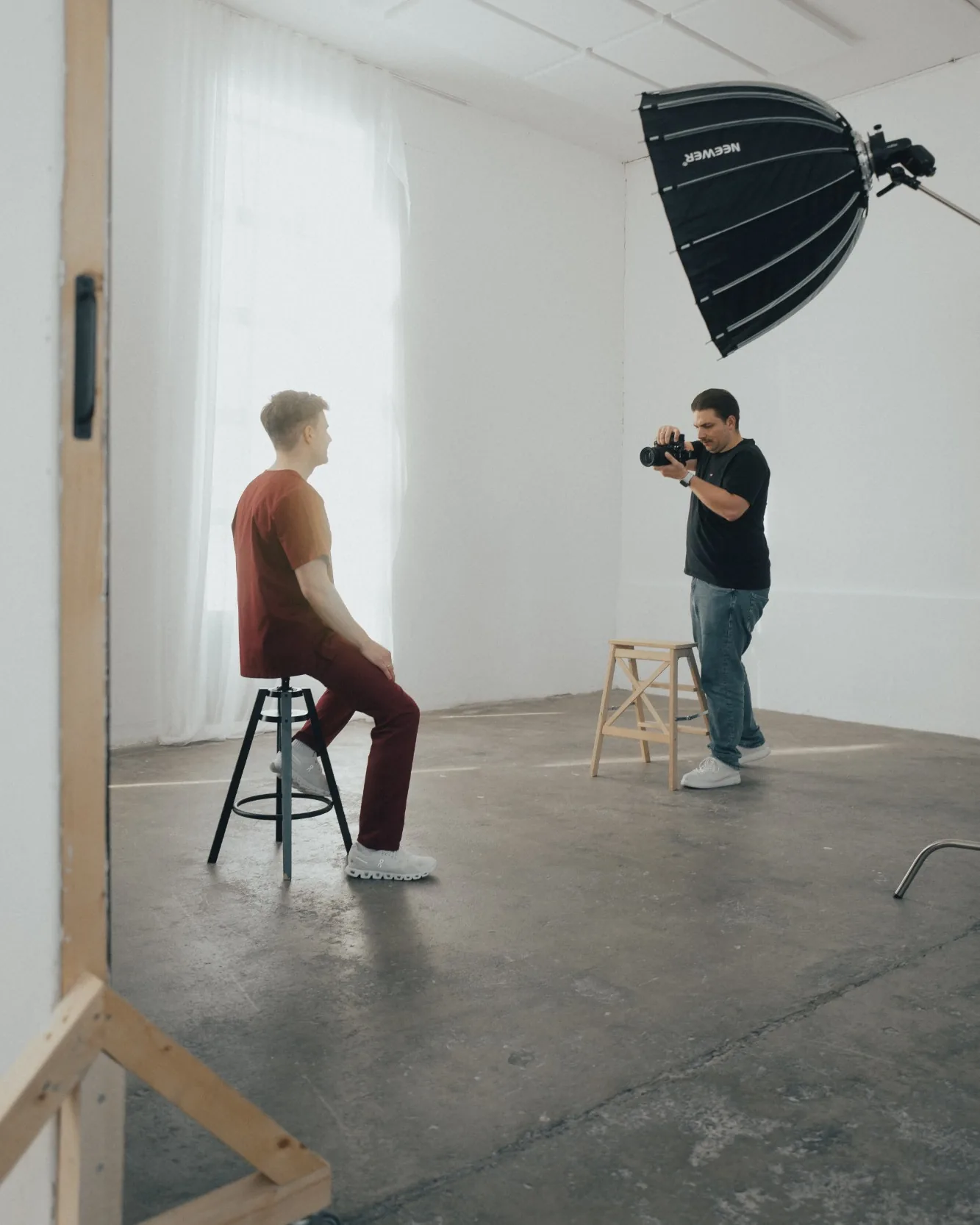 Nick Paysan fotografiert im hellen Studio einen Mann in weinroter Praxiskleidung, der auf einem Hocker sitzt