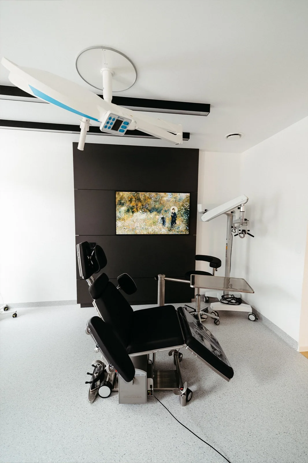 Behandlungsraum mit schwarzem Behandlungsstuhl und OP-Leuchte vor einer dunklen Wand